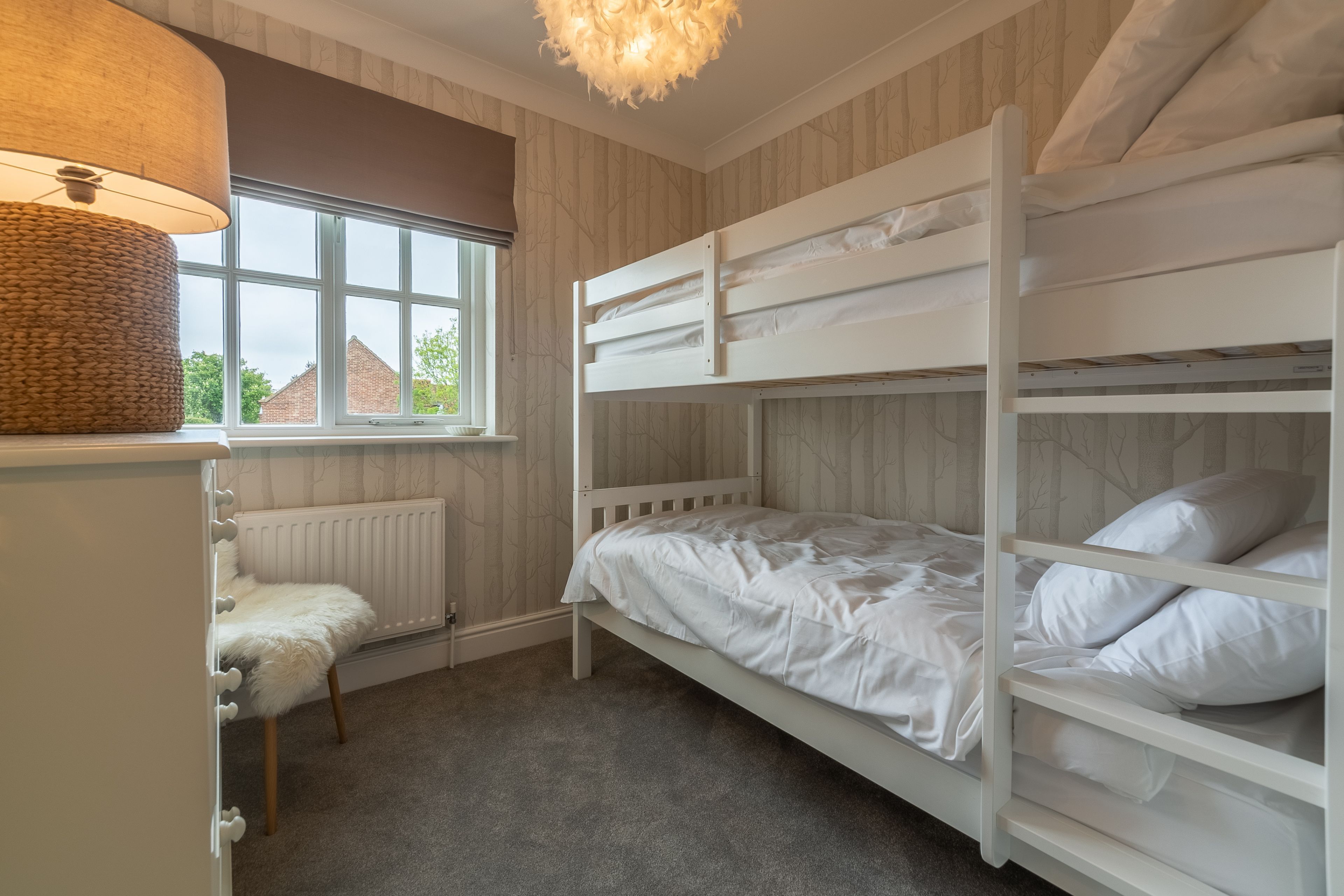 Een slaapkamer met een stapelbed, raam, radiator en lamp.