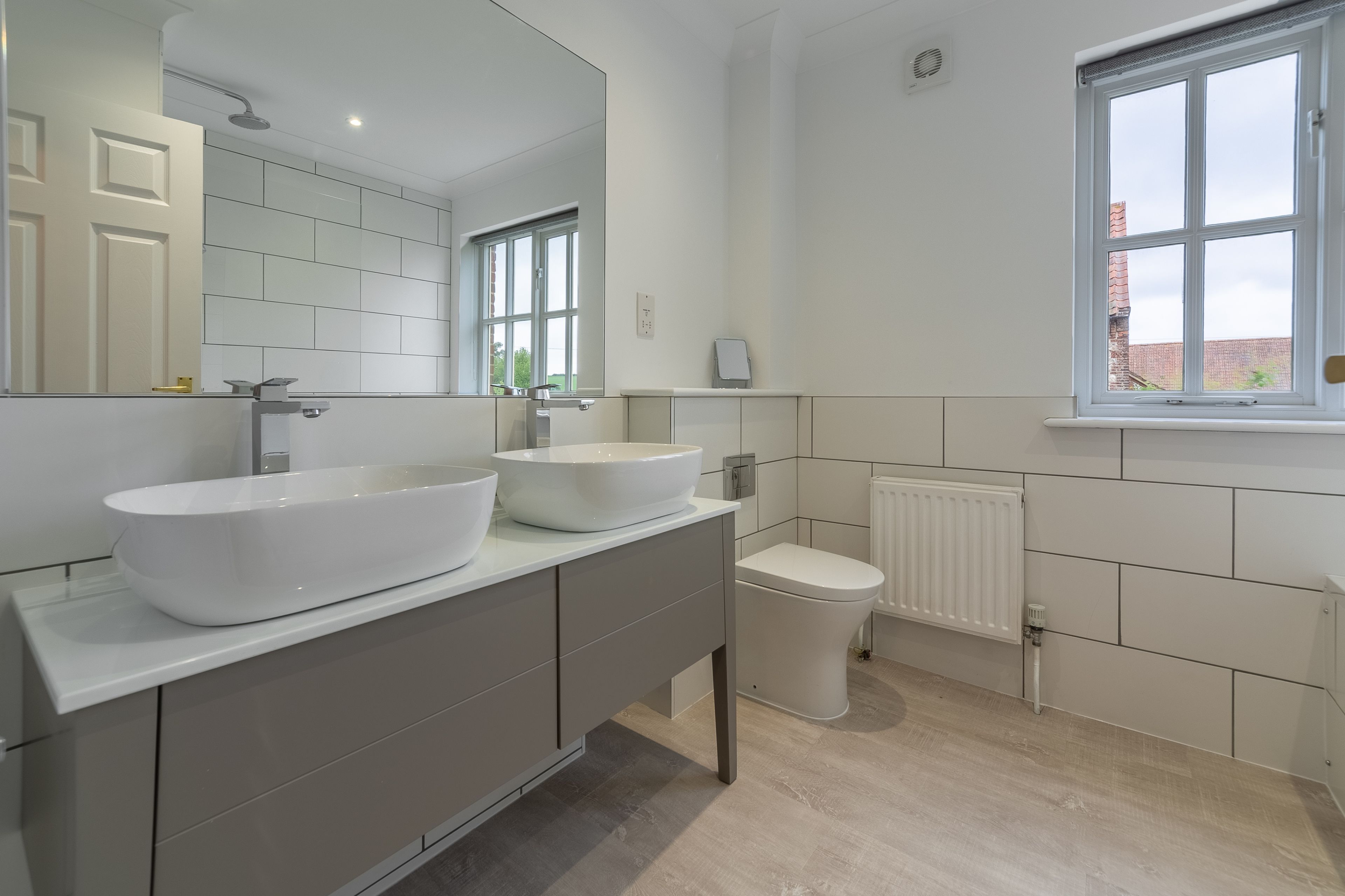 A modern bathroom with two large white sinks, a toilet, and a window.