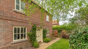 A brick house with a front door, windows, and a small garden with a lawn and shrubs.