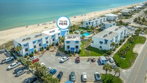 An aerial view of a coastal hotel with multiple buildings, a parking lot, and a beach in the background. - Located right on the beachfront, this beautiful well-appointed Villa offers you fabulous views. (St. George Island)