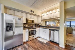 A modern kitchen with stainless steel appliances, white cabinetry, and a wooden floor.
