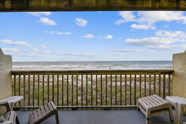 A balcony with a view of the ocean, wooden chairs, and a small table.