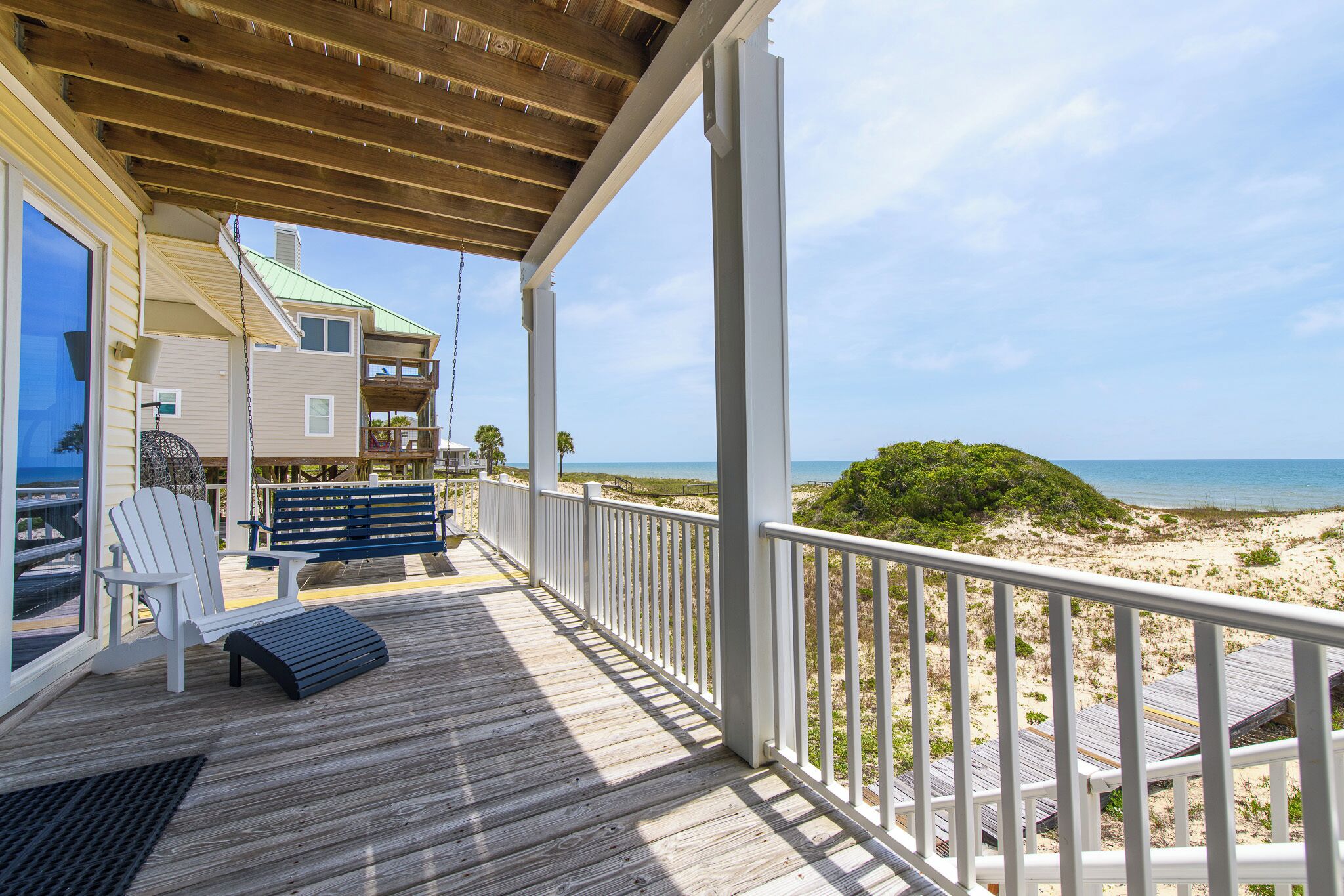 Eine Holzterrasse mit einer Bank und einem Stuhl, mit Blick auf einen Strand.