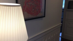 A room with a framed map of Paris, a lamp, and a small table with books and a vase. - Spacious 2 bedroom -MIT, Harvard, Central Square with parking* (Cambridge)