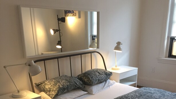A neatly arranged bedroom with a bed, two bedside lamps, a nightstand, a mirror, and a patterned rug. - Spacious 2 bedroom -MIT, Harvard, Central Square with parking* (Cambridge)