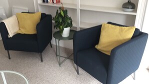 A living room with two dark blue armchairs, each with a yellow cushion, and a small round table with a potted plant. - Spacious 2 bedroom -MIT, Harvard, Central Square with parking* (Cambridge)