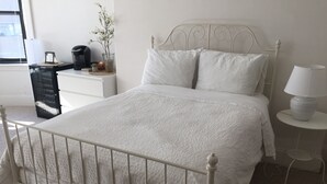 A neatly made bed with a white headboard, a bedside table with a lamp, and a small plant on the dresser. - Spacious 2 bedroom -MIT, Harvard, Central Square with parking* (Cambridge)
