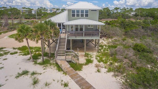 A beachfront house with a covered deck and a staircase leading to the entrance. - DELIGHT IN THE CHEERFUL AMUSEMENT of the sand crabs dancing in the moonlight. (St. George Island)