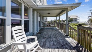 A wooden deck with a covered area, white chairs, and a view of the ocean. - DELIGHT IN THE CHEERFUL AMUSEMENT of the sand crabs dancing in the moonlight. (St. George Island)