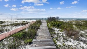 A wooden boardwalk leading to the beach, surrounded by sand and sparse vegetation. - DELIGHT IN THE CHEERFUL AMUSEMENT of the sand crabs dancing in the moonlight. (St. George Island)
