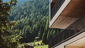 A modern building with a wooden facade and a balcony overlooking a forested valley. - Hotel Mea Via (Castelrotto)