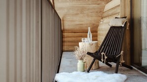 A wooden interior with a black lounge chair, a white fur rug, and a vase with dried plants. - Hotel Mea Via (Castelrotto)