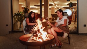 Two people sitting by a fire pit in a well-lit indoor space with modern decor and plants. - Hotel Mea Via (Castelrotto)