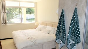 A bedroom with a bed, a window, a bathroom, and towels hanging on the wall. - Lagoon Terrace 14 (Plettenberg Bay)