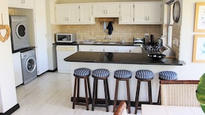 A kitchen with a central island, bar stools, a washing machine, a microwave, and a sink. - Lagoon Terrace 14 (Plettenberg Bay)