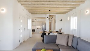 Una sala de estar moderna con un sofá seccional gris, una mesa de centro de madera con una pera verde, y una cocina al fondo.
