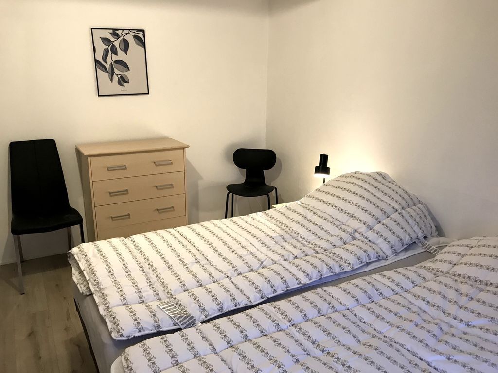 Une chambre à coucher comprenant un lit, une commode, une chaise et une lampe fixée au mur.