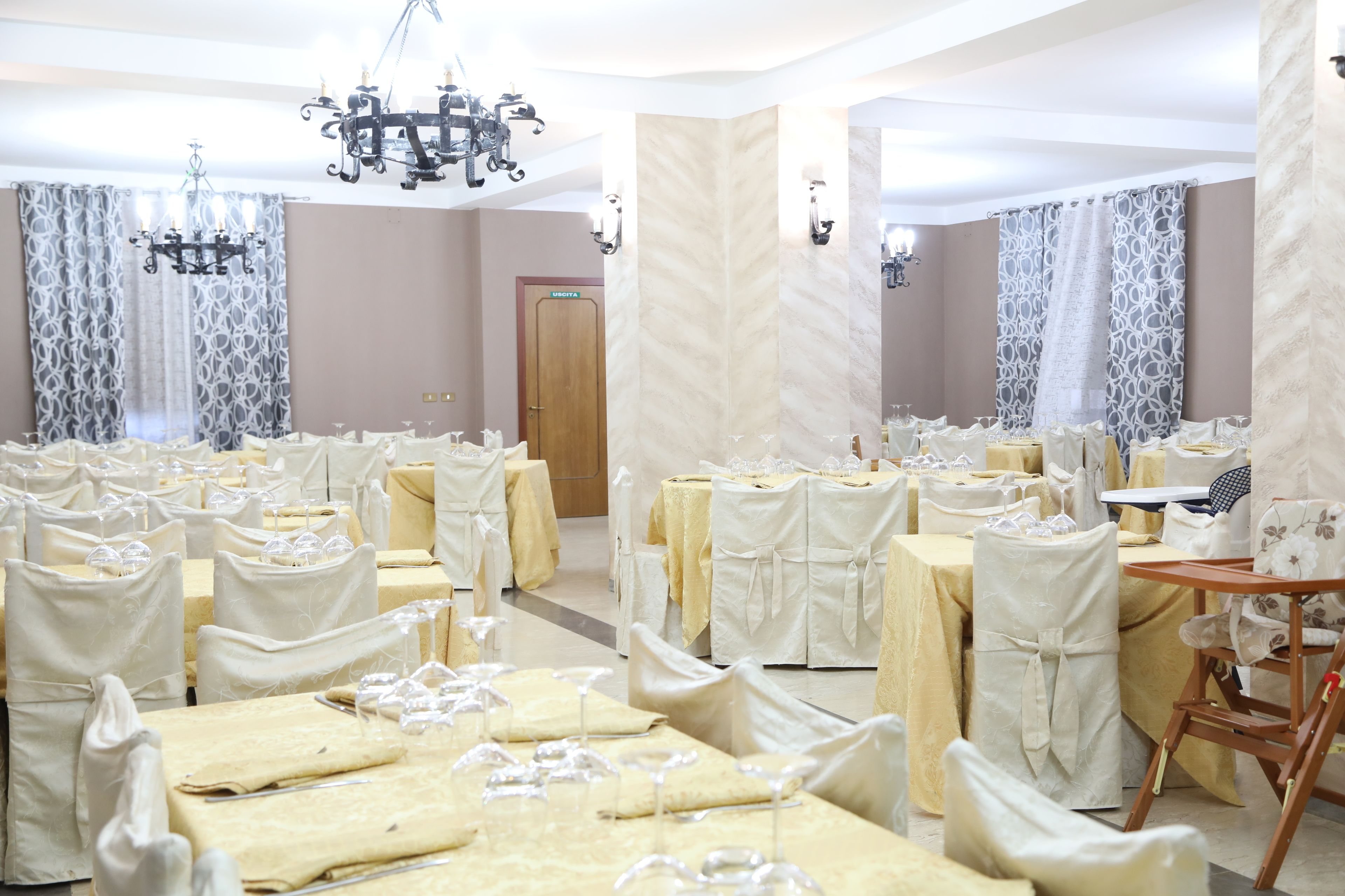 A banquet hall with multiple round tables, each covered with white tablecloths and set with wine glasses.