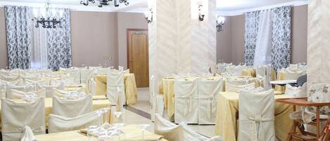 A banquet hall with multiple round tables, each covered with white tablecloths and set with wine glasses.