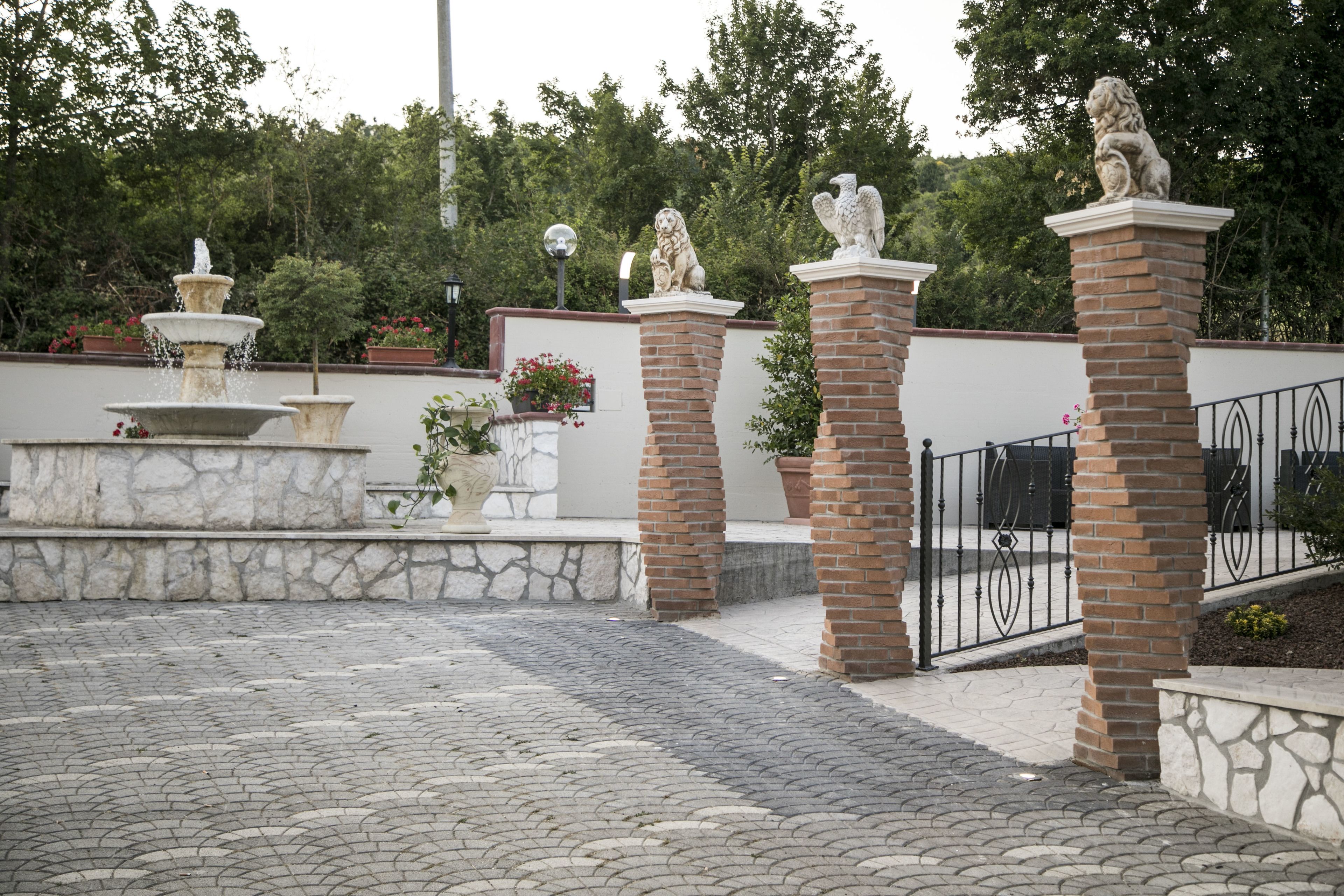 A courtyard with a fountain, stone planters, and statues on brick pillars.
