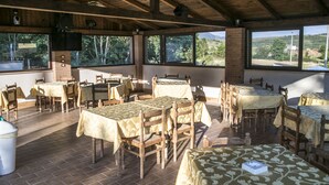 An outdoor dining area with wooden tables and chairs, large windows, and a brick wall. - Hotel Ristorante Il Giardino (Cagnano Amiterno)