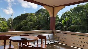 Un espacio de estar techado al aire libre con una mesa y sillas, con vistas a un exuberante jardín con palmeras.