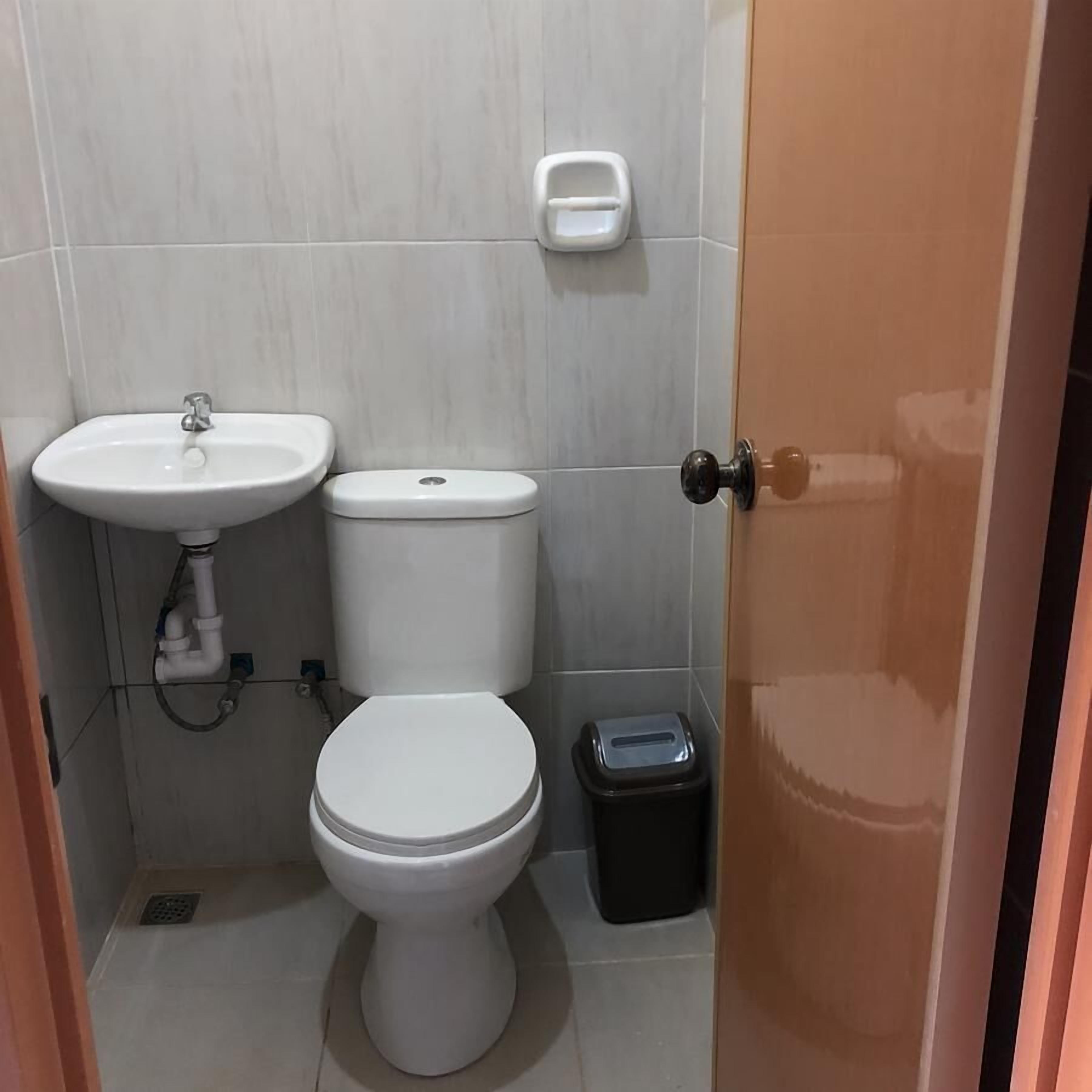 Et lille badeværelse med toilet, håndvask og skraldespand.
