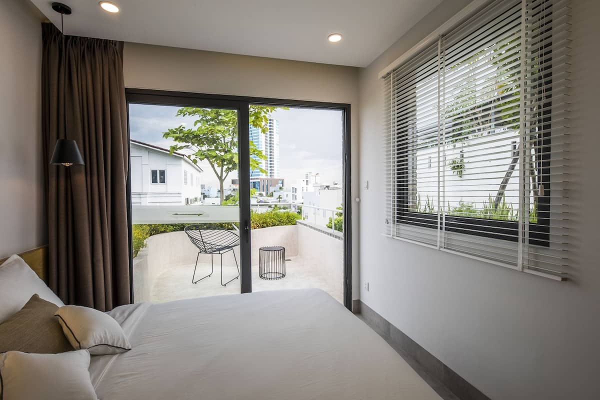 A bedroom with a large bed, a view of the outside, and a balcony with a chair and table.