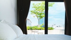 A bedroom with a bed, a view of a tree and buildings through a window. - Green Peace Da Nang (Da Nang)