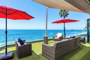 Eine Terrasse am Meer mit Korbmöbeln und roten Sonnenschirmen, mit Blick auf den Ozean.