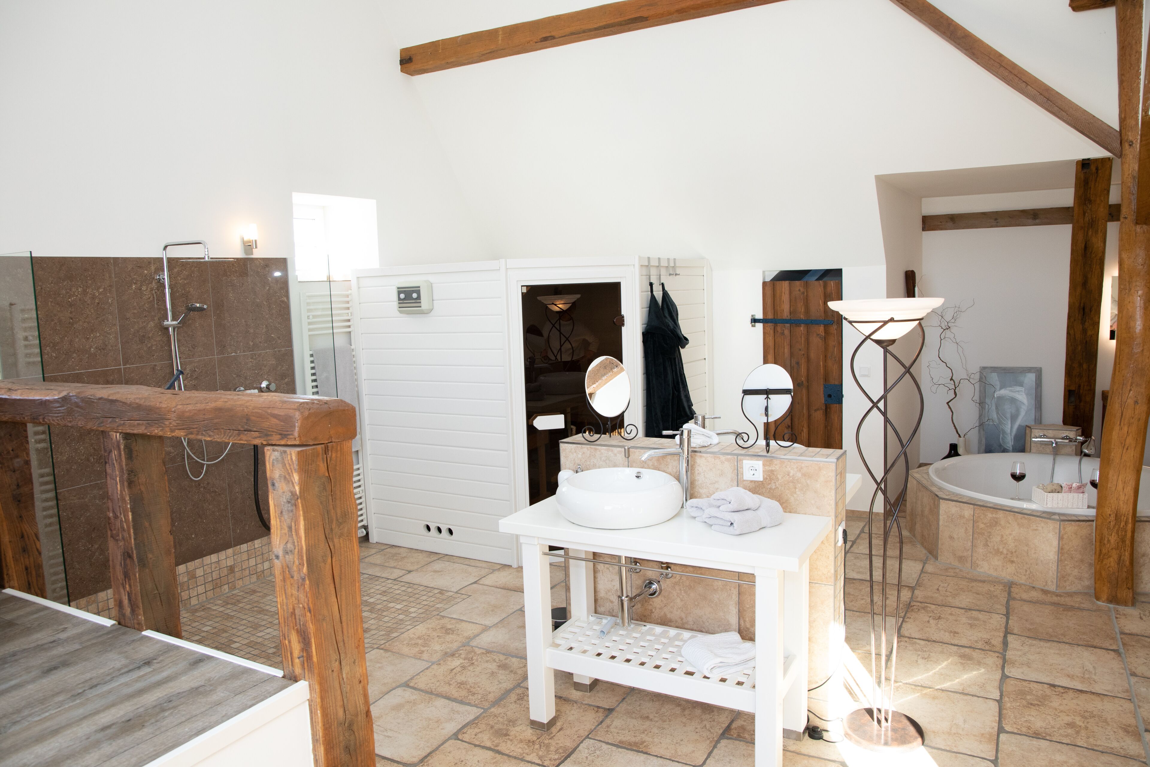 A bathroom with a wooden vanity, a sink, a mirror, a bathtub, and a floor lamp.