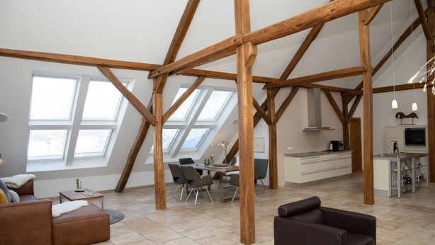 Un loft amplio con techos altos, vigas de madera a la vista, una zona de comedor, una cocina y ventanas grandes.