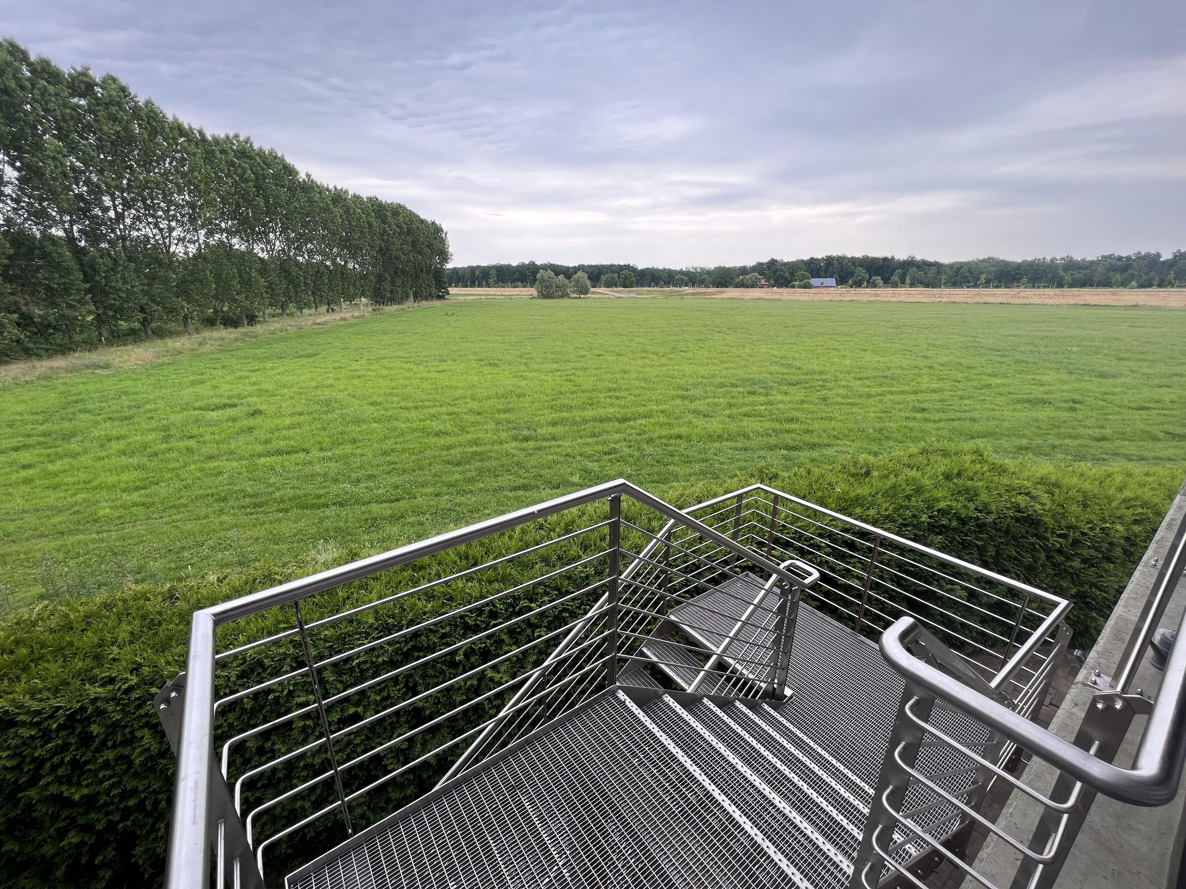 Een metalen trap die leidt naar een groen veld met bomen op de achtergrond.