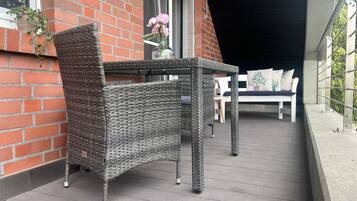 A wicker table and chair set on a balcony with a brick wall and a window.