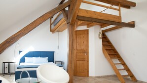 Un dormitorio con una cama, una bañera blanca, una escalera de madera y una puerta de madera.