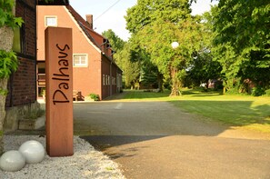 A building with a sign reading "Dallhaus" and a paved driveway leading to a grassy area with trees. - Hof Dalhaus (Luedinghausen)