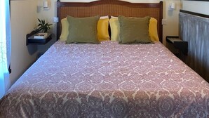 A bedroom with a wooden ceiling, a bed with patterned bedding, two bedside tables with lamps, and a nightstand with a plant. - Hotel y Apartamentos Son de Mar (Villaviciosa)