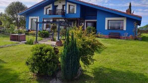A two-story house with a red roof and blue exterior walls. It has a balcony on the upper floor and a small garden area in front. - Hotel y Apartamentos Son de Mar (Villaviciosa)