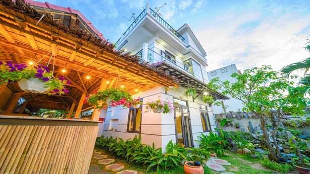 A modern two-story house with a covered patio area, hanging flower baskets, and a well-maintained garden. - Hoi An Garden Sea Homestay (Da Nang)