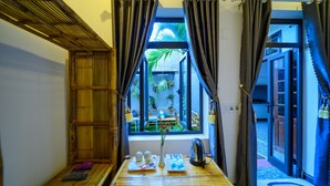 A room with a bamboo ceiling, a window with curtains, a table with a tray of items, and a view of a garden outside. - Hoi An Garden Sea Homestay (Da Nang)