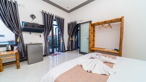 A hotel room with a bed, a desk, a minibar, a television, and a bathroom with a mirror and towel rack. - Hoi An Garden Sea Homestay (Da Nang)