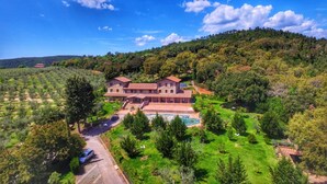 Un gran edificio de piedra de dos pisos con piscina, rodeado de vegetación exuberante y colinas.