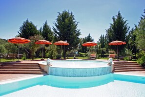 Ein Swimmingpool mit roten Sonnenschirmen, umgeben von Bäumen und einer Pflasterterrasse.