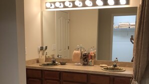 A bathroom with a vanity, a large mirror, and a lighted vanity area.