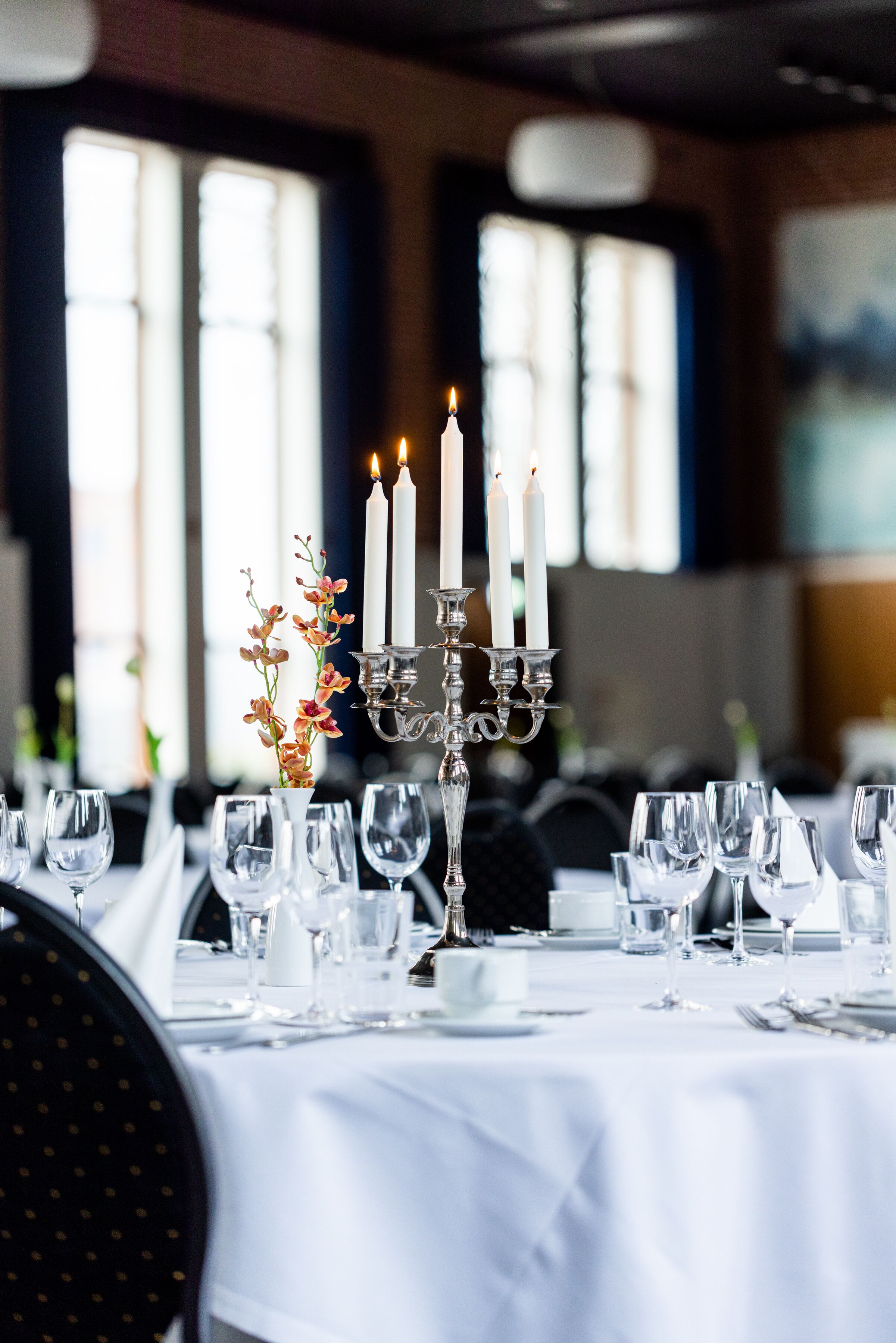 A table set for dining with candles, clear glasses, and a vase with flowers.