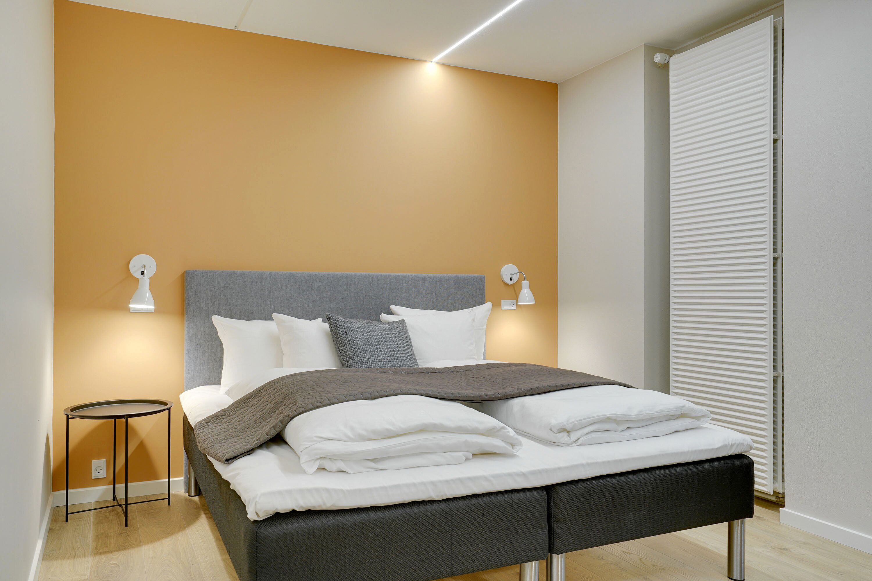 Ein modernes Schlafzimmer mit Bett, Nachttischlampen und Heizkörper.