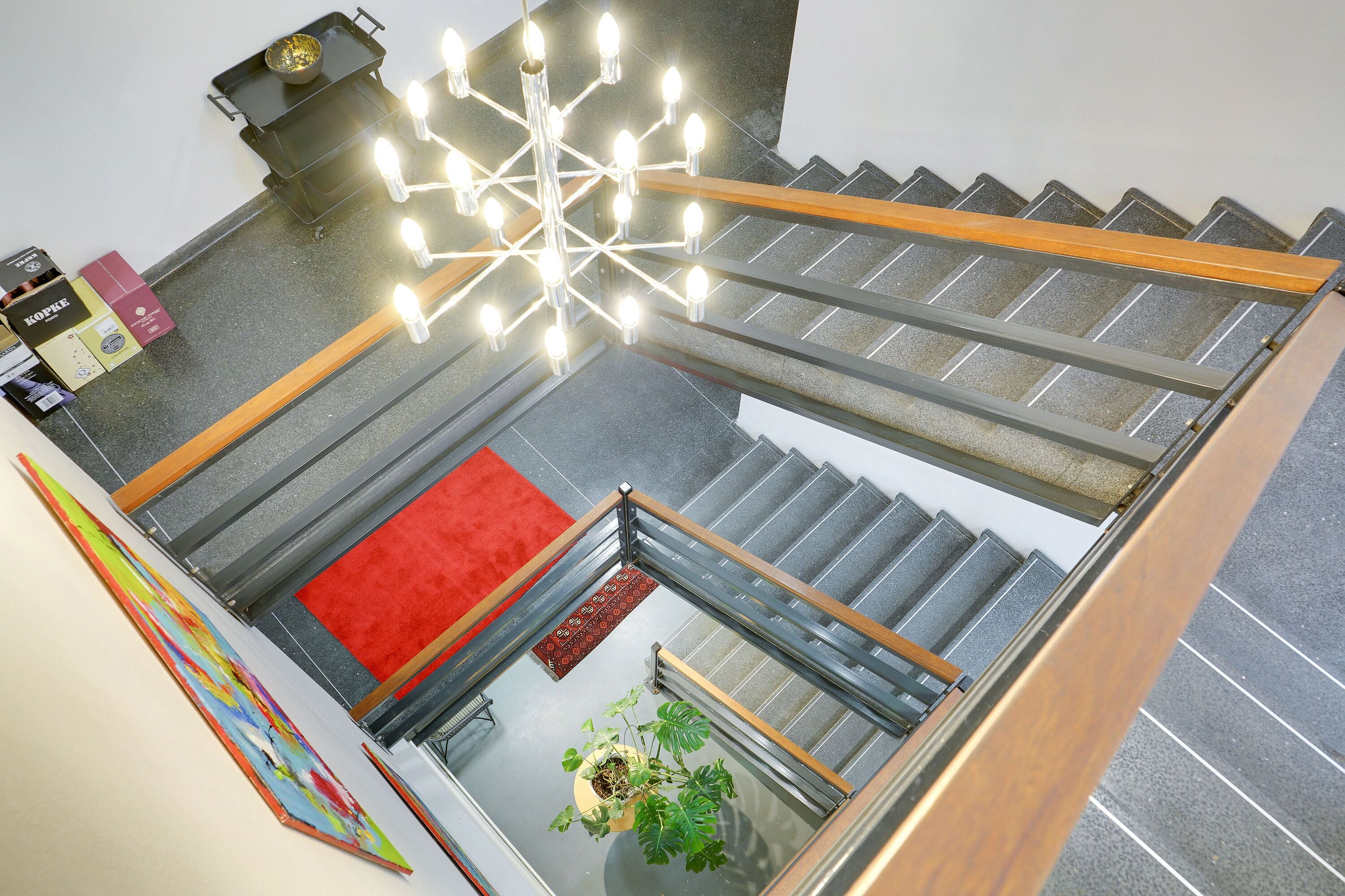 A staircase with a glass railing, a red carpet, and a hanging light fixture.