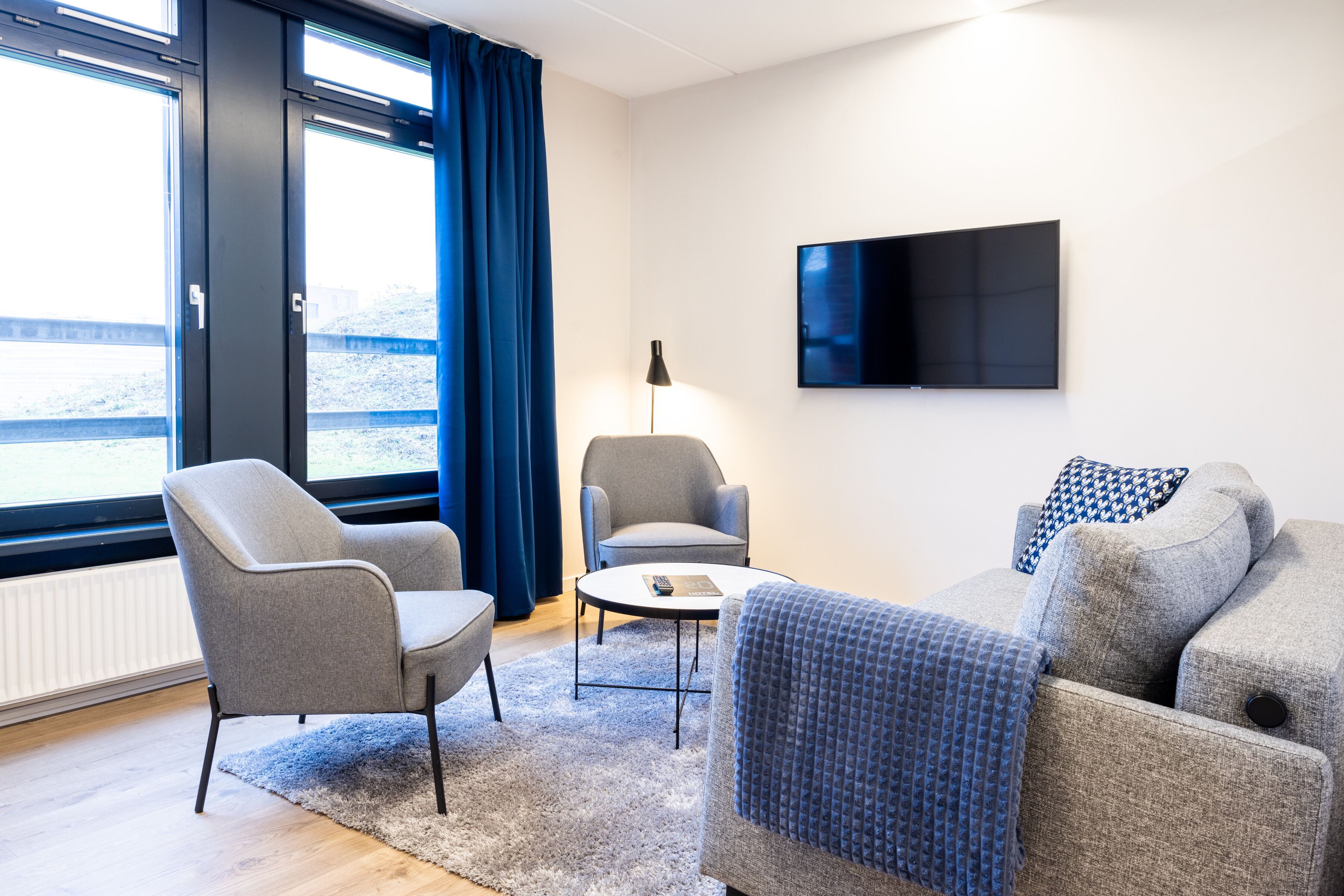 Un salon moderne comprenant un canapé, deux fauteuils, une table basse et un téléviseur à écran plat fixé au mur.