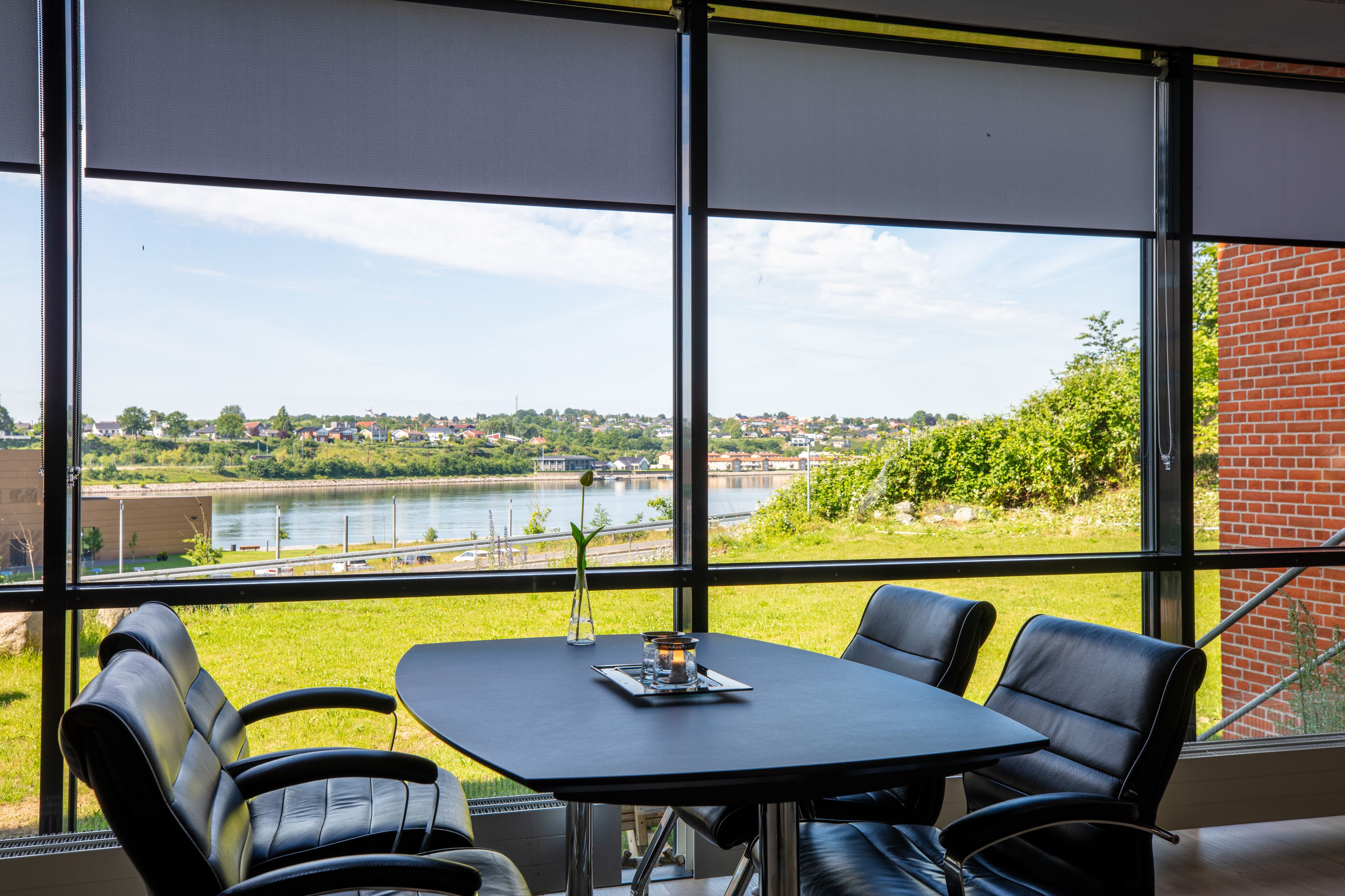 Une pièce avec une table et des chaises, donnant sur une grande fenêtre qui offre une vue sur une rivière et la verdure environnante.