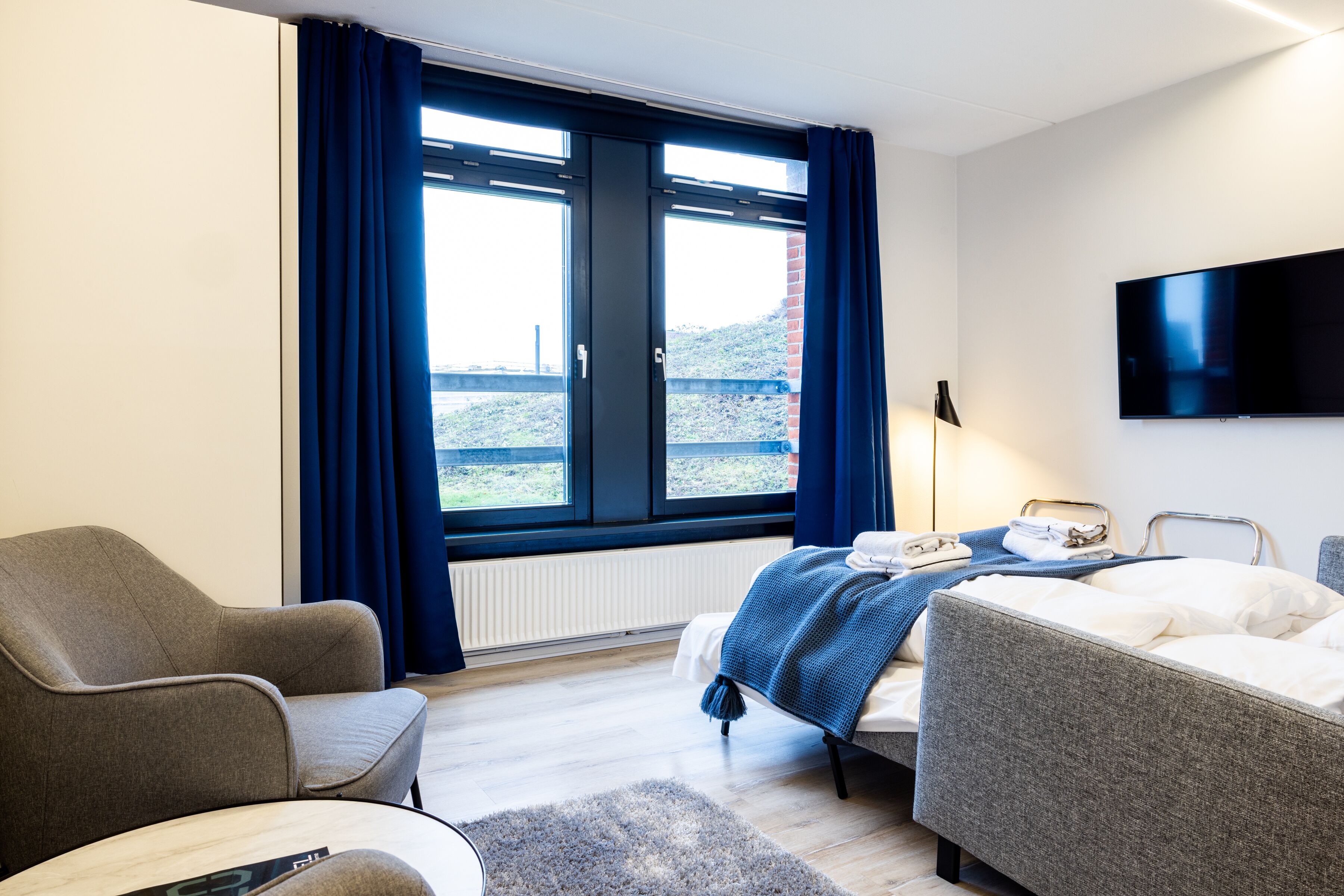 A modern hotel room with a bed, a chair, a desk, and a TV.